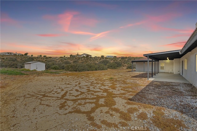 yard at dusk featuring an outdoor structure and a carport