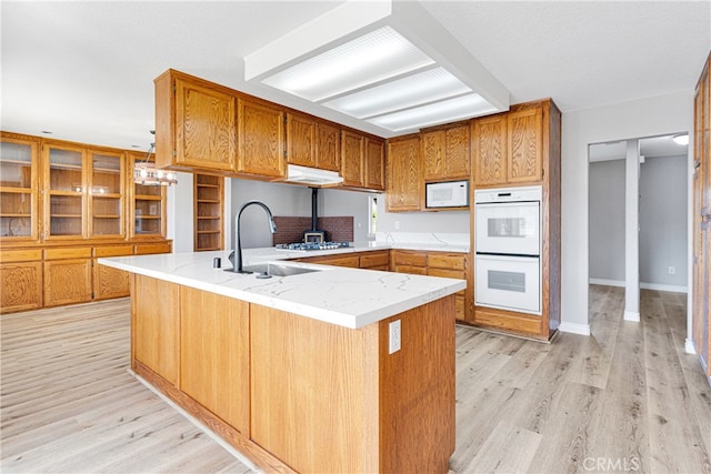 kitchen with light wood-type flooring, white appliances, kitchen peninsula, and sink