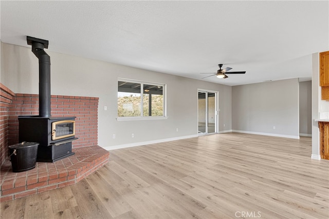 unfurnished living room with light wood-type flooring, a textured ceiling, ceiling fan, and a wood stove