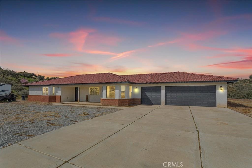 7372 Barker Rd, Oak Hills, CA 92344 - view of front facade with a garage, concrete driveway, brick siding, a tile roof, and stucco siding