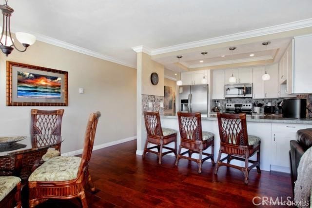 kitchen with white cabinetry, dark hardwood / wood-style floors, crown molding, pendant lighting, and appliances with stainless steel finishes