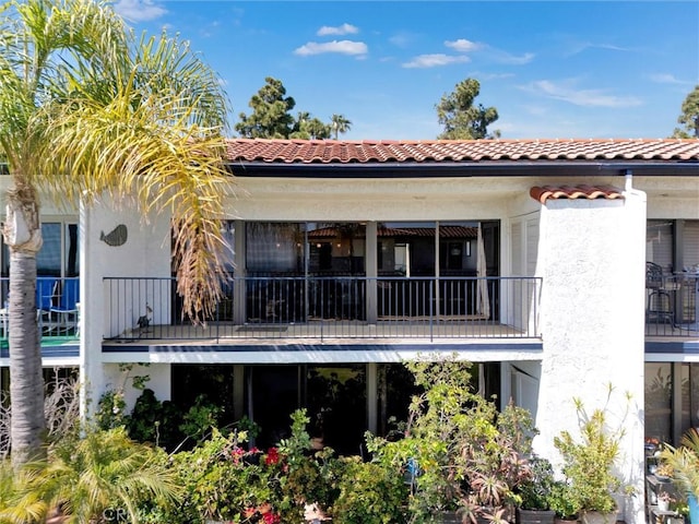 rear view of house with a tile roof, a balcony, and stucco siding