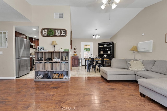 living room with ceiling fan with notable chandelier, lofted ceiling, and light hardwood / wood-style flooring