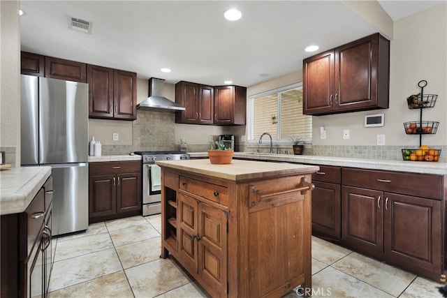 kitchen featuring sink, a kitchen island, wall chimney range hood, appliances with stainless steel finishes, and dark brown cabinetry