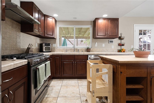 kitchen featuring light tile patterned floors, sink, backsplash, wall chimney range hood, and stainless steel stove