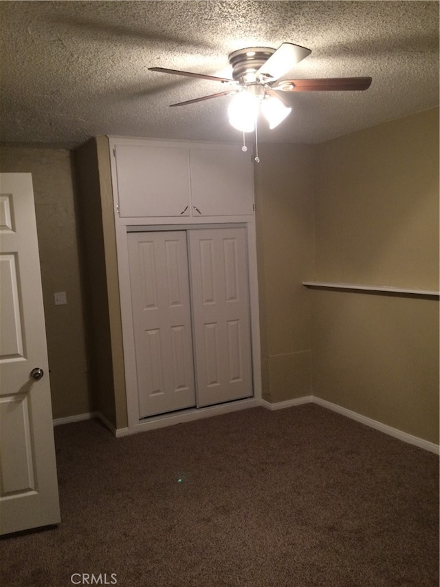 unfurnished bedroom with a textured ceiling, dark colored carpet, ceiling fan, and a closet