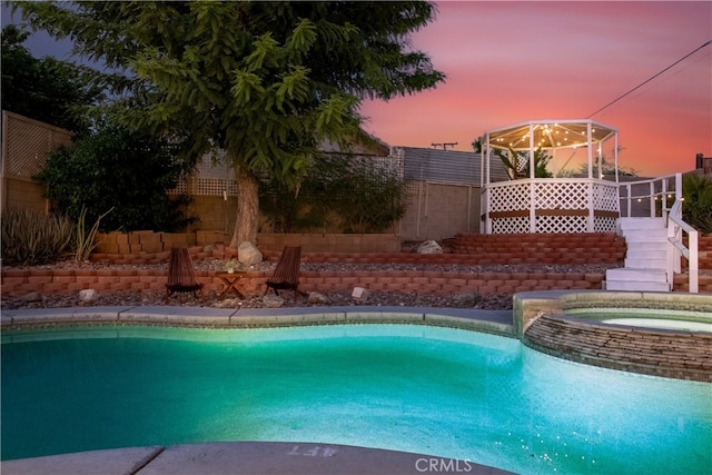 pool at dusk with an in ground hot tub