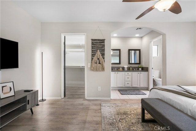 bedroom with a closet, light hardwood / wood-style floors, a walk in closet, ensuite bathroom, and ceiling fan