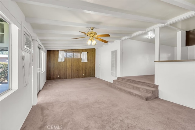 empty room with beamed ceiling, wooden walls, light carpet, and ceiling fan