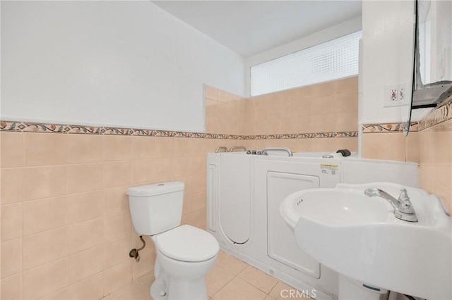 bathroom with toilet, sink, tile walls, and tile patterned flooring