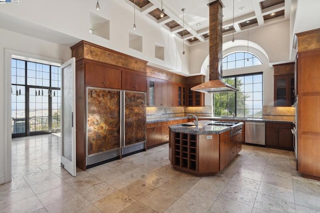 kitchen with a center island with sink, a towering ceiling, appliances with stainless steel finishes, and coffered ceiling