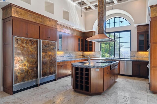 kitchen featuring a towering ceiling, an island with sink, coffered ceiling, and appliances with stainless steel finishes