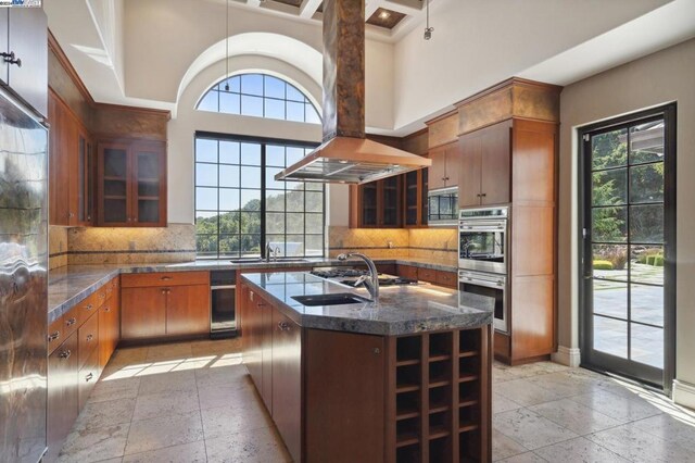 kitchen featuring island exhaust hood, a towering ceiling, a kitchen island with sink, and a healthy amount of sunlight