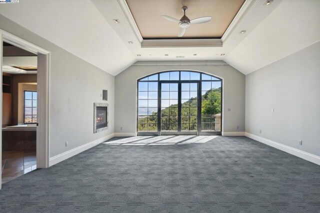 unfurnished living room featuring a tray ceiling, vaulted ceiling, ceiling fan, crown molding, and dark colored carpet