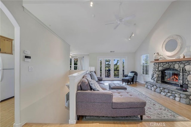 living room featuring ceiling fan, light hardwood / wood-style floors, a fireplace, and high vaulted ceiling