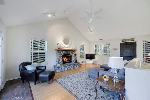 living room featuring ceiling fan, rail lighting, high vaulted ceiling, light hardwood / wood-style floors, and a fireplace