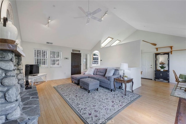 living room with high vaulted ceiling, track lighting, ceiling fan, a fireplace, and light hardwood / wood-style floors