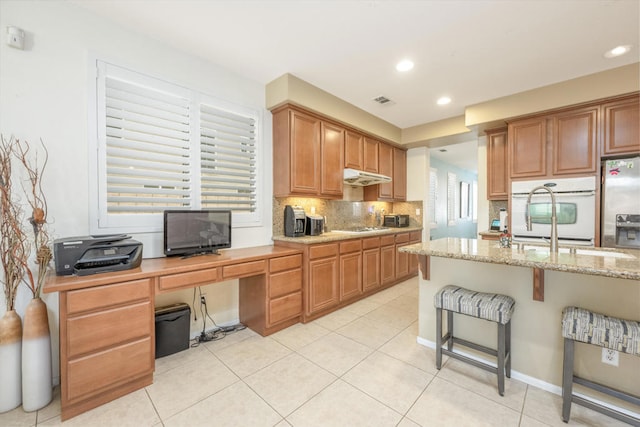 kitchen with light tile patterned floors, tasteful backsplash, appliances with stainless steel finishes, a breakfast bar area, and light stone countertops