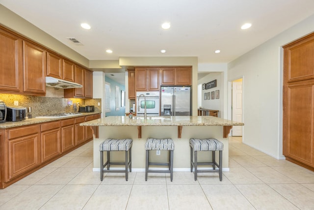 kitchen featuring a kitchen breakfast bar, a center island with sink, white appliances, and light stone counters