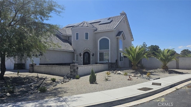 view of front of property featuring stucco siding, fence, a tile roof, and roof mounted solar panels