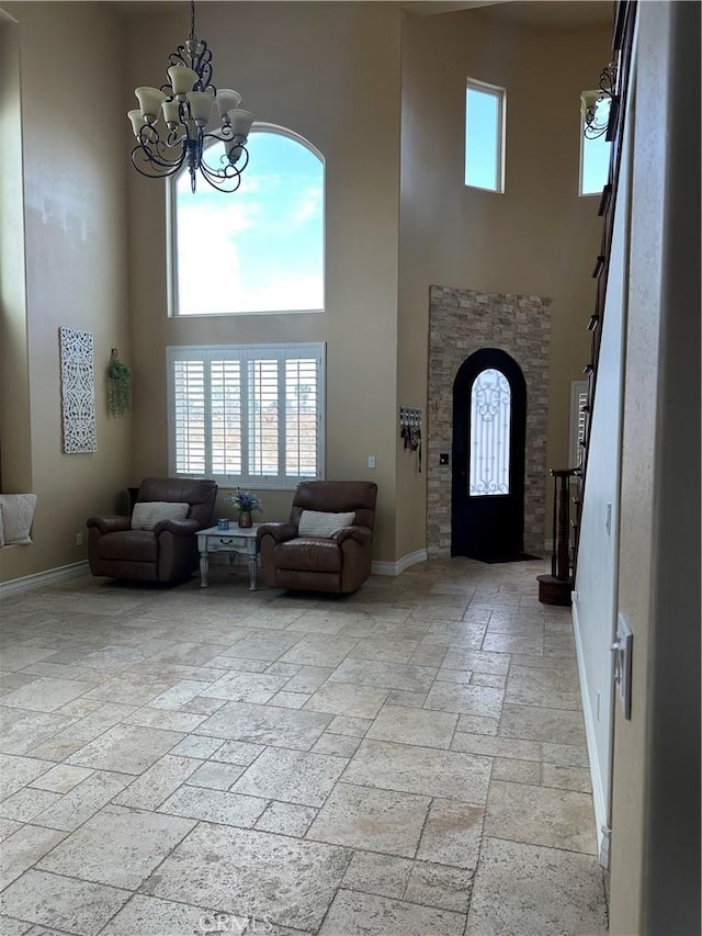 entrance foyer featuring a chandelier, a high ceiling, stone tile floors, and baseboards