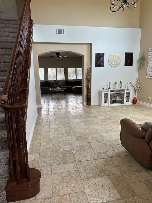 living room featuring stone tile floors, arched walkways, baseboards, stairway, and a high ceiling