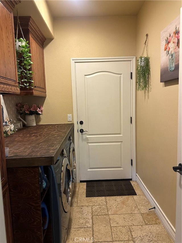 clothes washing area with cabinet space, stone tile floors, washer and clothes dryer, and baseboards