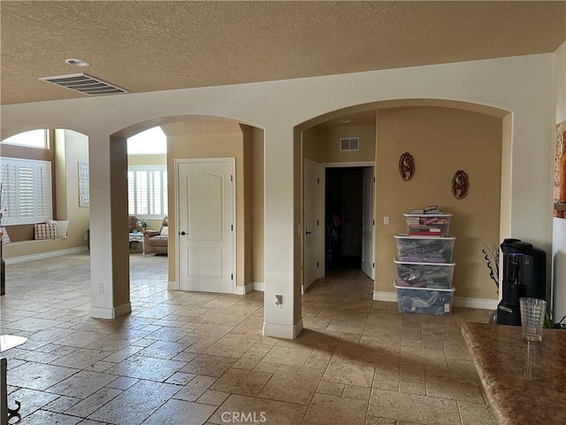 interior space featuring stone tile floors, a textured ceiling, visible vents, and baseboards