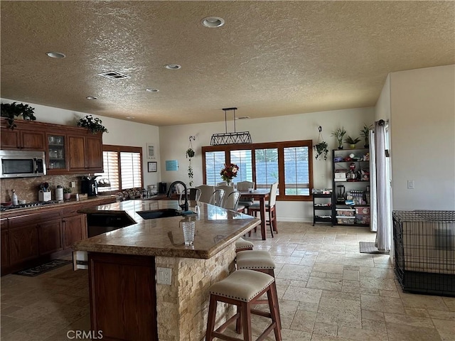 kitchen featuring stone tile flooring, stainless steel microwave, visible vents, a sink, and a kitchen bar