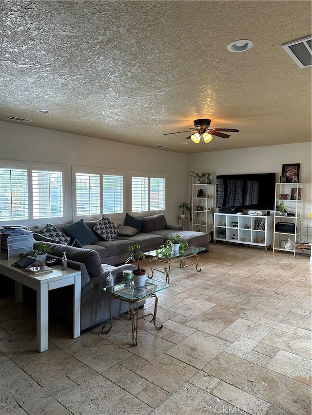 living area with a ceiling fan, visible vents, a textured ceiling, and stone tile floors