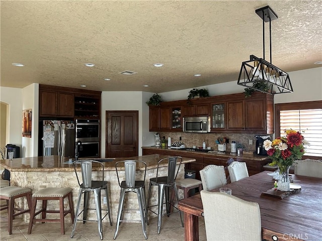 kitchen with appliances with stainless steel finishes, glass insert cabinets, backsplash, and a kitchen breakfast bar