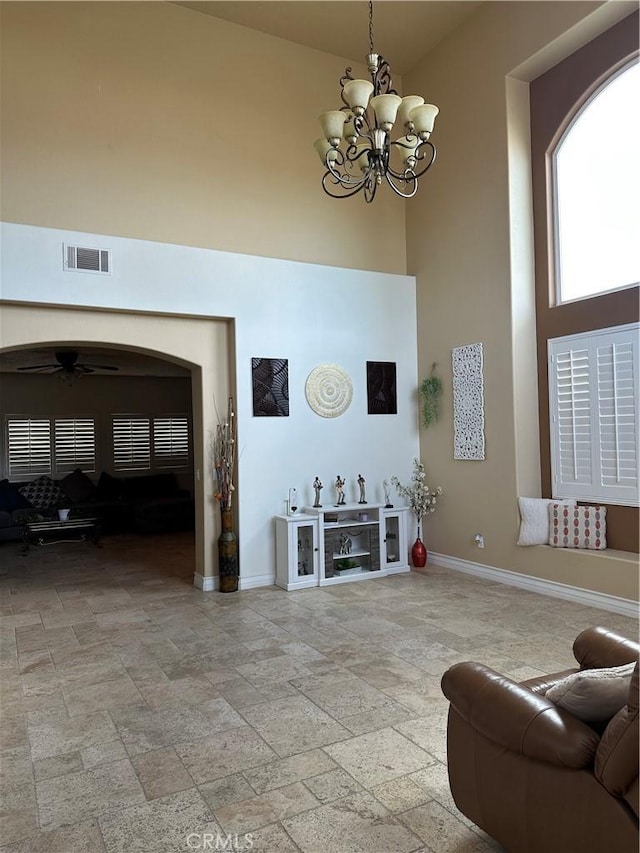 living area with visible vents, a towering ceiling, stone finish flooring, baseboards, and ceiling fan with notable chandelier