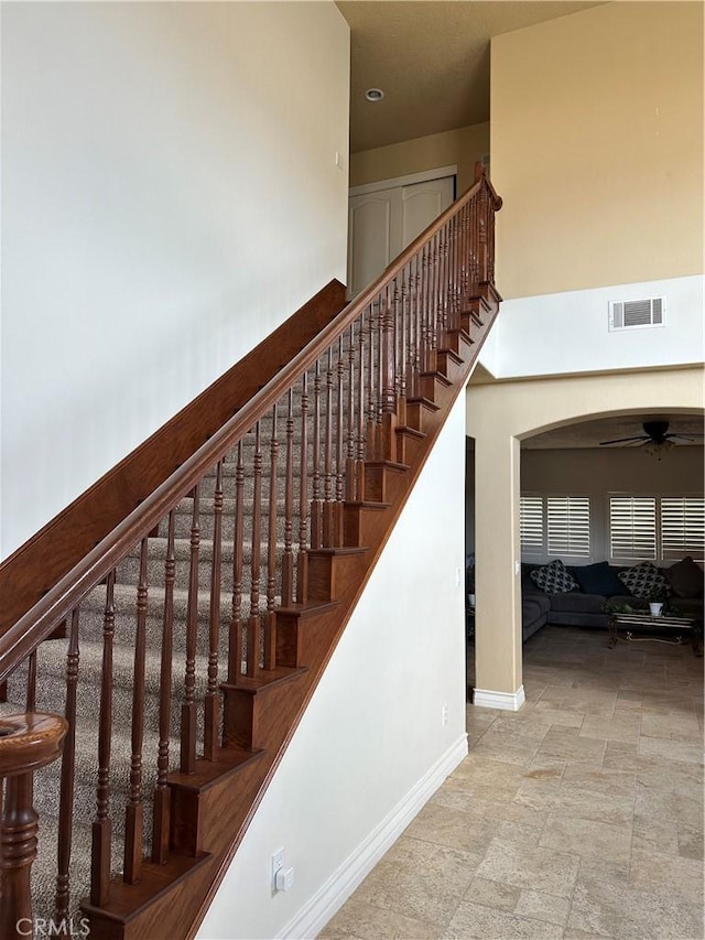 stairs with arched walkways, visible vents, a high ceiling, ceiling fan, and baseboards