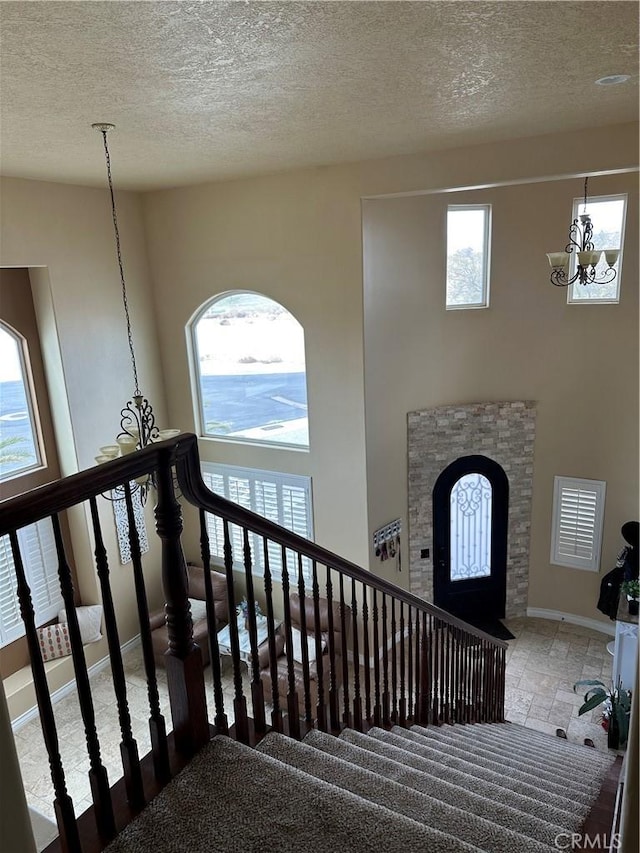 stairs with baseboards, a high ceiling, a chandelier, and a textured ceiling