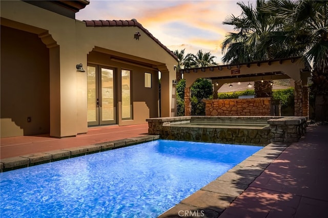 pool at dusk with pool water feature, an in ground hot tub, a patio, and french doors