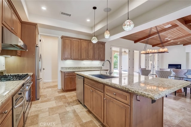 kitchen with sink, an island with sink, appliances with stainless steel finishes, beamed ceiling, and a kitchen bar