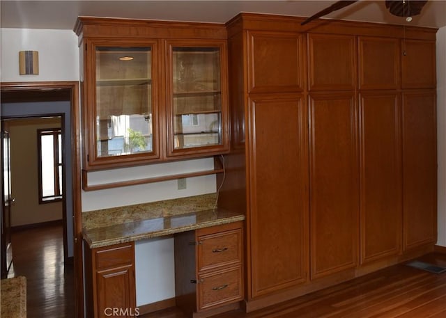 kitchen with light stone countertops, built in desk, and dark wood-type flooring