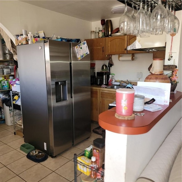 kitchen with light tile patterned floors, brown cabinetry, a sink, and stainless steel fridge with ice dispenser