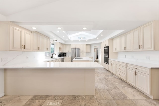 kitchen featuring stainless steel appliances, a tray ceiling, kitchen peninsula, and cream cabinetry