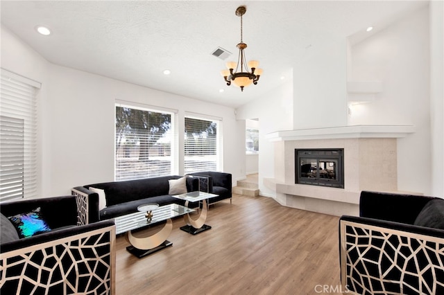 living room featuring lofted ceiling, a fireplace, hardwood / wood-style floors, and a notable chandelier