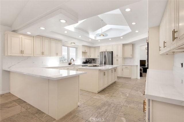 kitchen with a center island, kitchen peninsula, stainless steel refrigerator, a raised ceiling, and light stone countertops