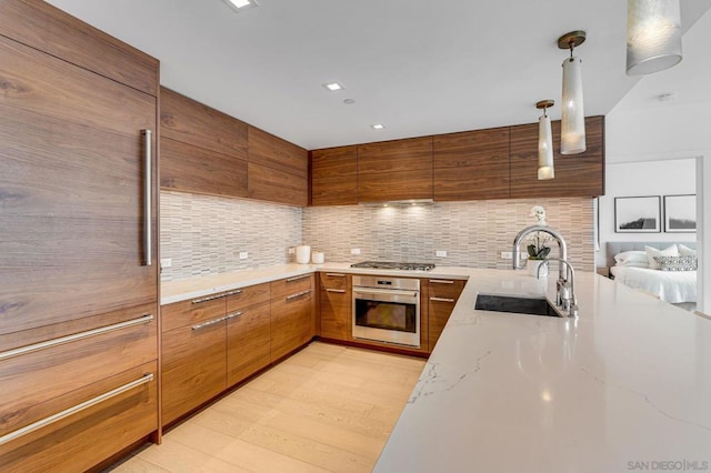 kitchen with appliances with stainless steel finishes, tasteful backsplash, light wood-type flooring, hanging light fixtures, and sink