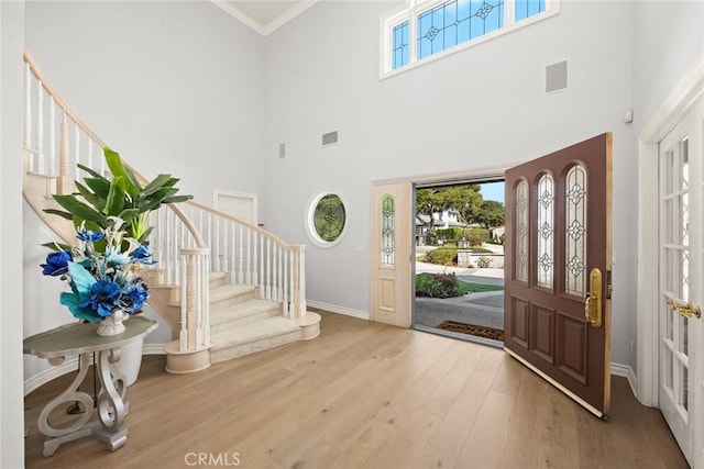 foyer with a towering ceiling, ornamental molding, and hardwood / wood-style flooring