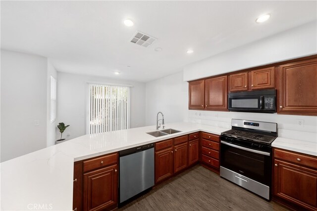 kitchen with dark wood-type flooring, kitchen peninsula, light stone countertops, stainless steel appliances, and sink