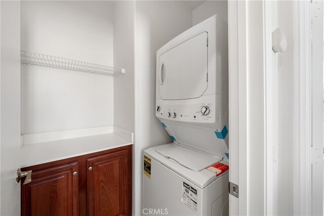 laundry room featuring cabinets and stacked washing maching and dryer