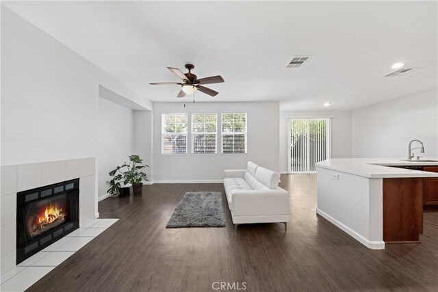 unfurnished living room with ceiling fan, a tile fireplace, hardwood / wood-style floors, and sink