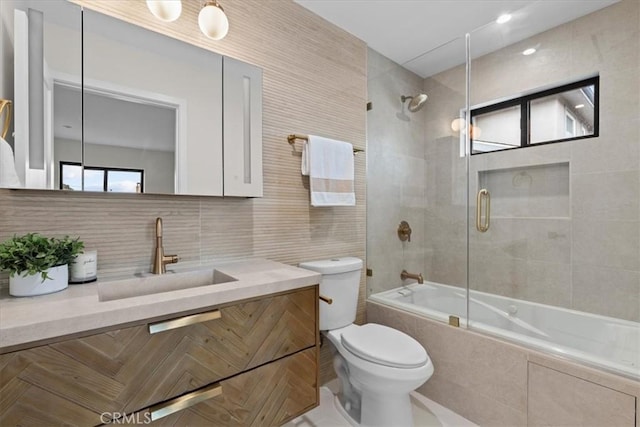 full bathroom featuring toilet, tasteful backsplash, combined bath / shower with glass door, tile walls, and vanity