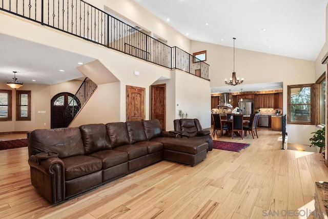 living room featuring a notable chandelier, light hardwood / wood-style floors, and high vaulted ceiling