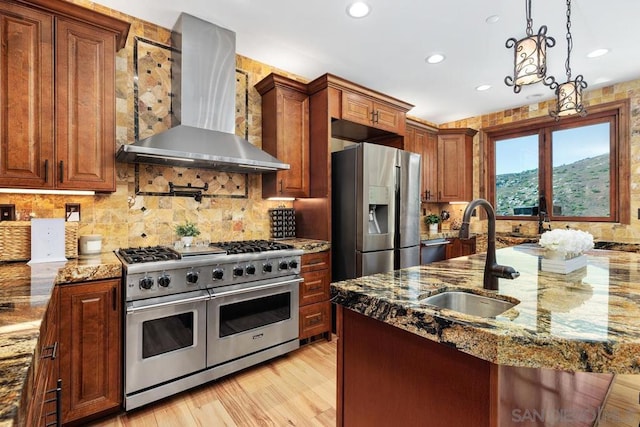 kitchen with wall chimney range hood, light wood-type flooring, sink, stainless steel appliances, and hanging light fixtures