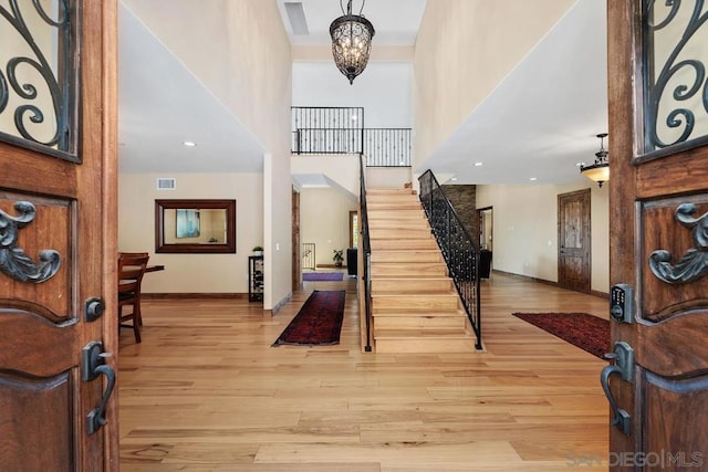 entryway featuring a notable chandelier, a towering ceiling, and light hardwood / wood-style flooring